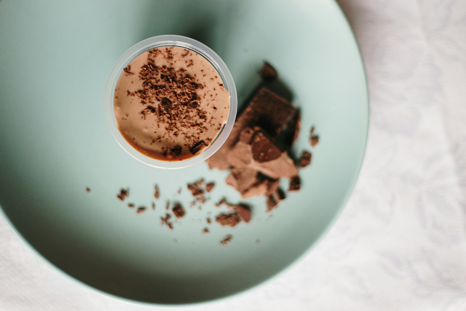 A cup of creamy chocolate mousse topped with chocolate shavings on a pale green plate