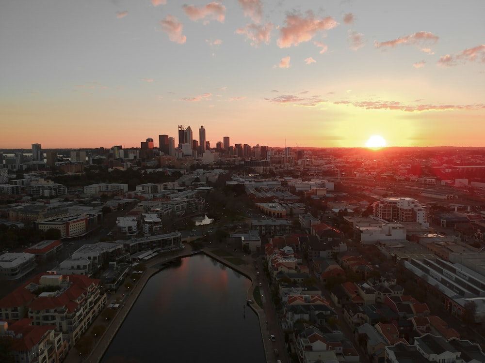 the sun is setting over a city with a body of water