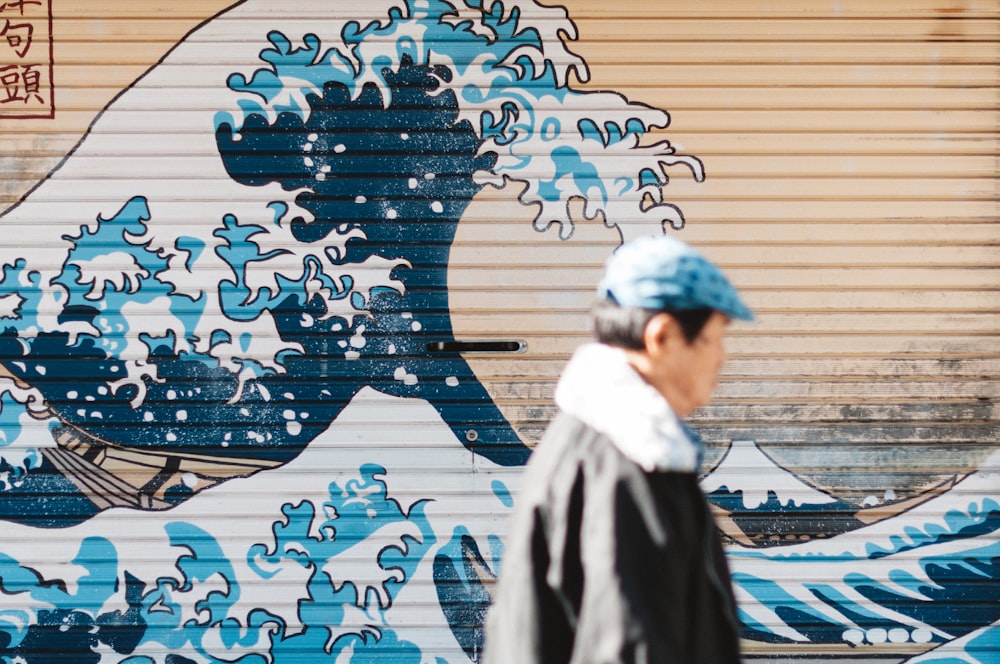 man walking beside The Great Wave Off Kanagawa painting on metal garage door