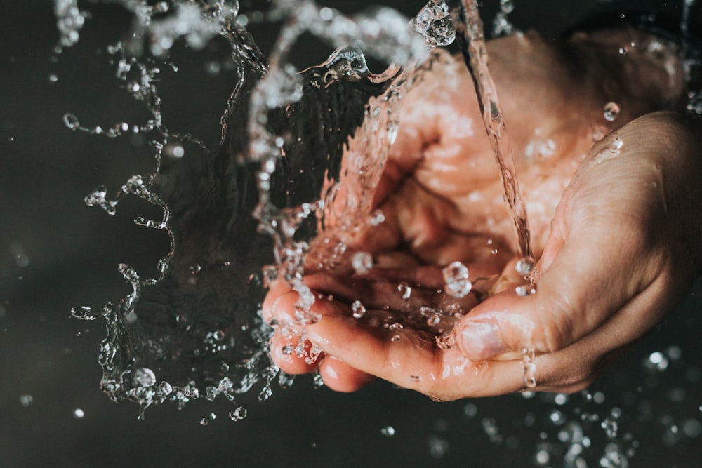 uma pessoa segurando suas mãos sob um fluxo de água