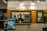 A counter with the name 'Janji Jiwa' above it, featuring a wooden panel design. Two people are behind the counter; they appear to work there. To the left, there are promotional posters, including one advertising a 10% cashback offer with GoPay. There are hanging lights and green plants adding to the decor.