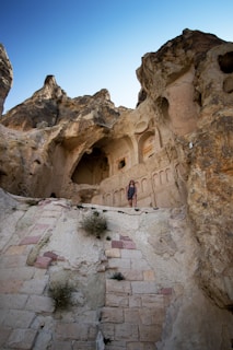 Action shot of Lara Croft cosplay climbing ancient ruins under a bright blue sky.