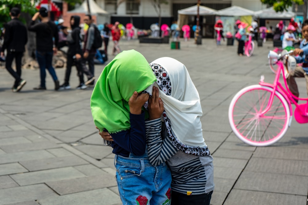 two women in headscarves standing beside pink bicycle