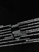 Bright white text is projected onto a dark surface, with several lines overlapping in various orientations. The text appears fragmented and partially obscured by shadows, creating an abstract and mysterious visual effect.
