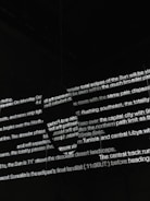 Bright white text is projected onto a dark surface, with several lines overlapping in various orientations. The text appears fragmented and partially obscured by shadows, creating an abstract and mysterious visual effect.