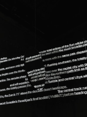 Bright white text is projected onto a dark surface, with several lines overlapping in various orientations. The text appears fragmented and partially obscured by shadows, creating an abstract and mysterious visual effect.