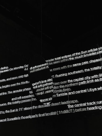 Bright white text is projected onto a dark surface, with several lines overlapping in various orientations. The text appears fragmented and partially obscured by shadows, creating an abstract and mysterious visual effect.