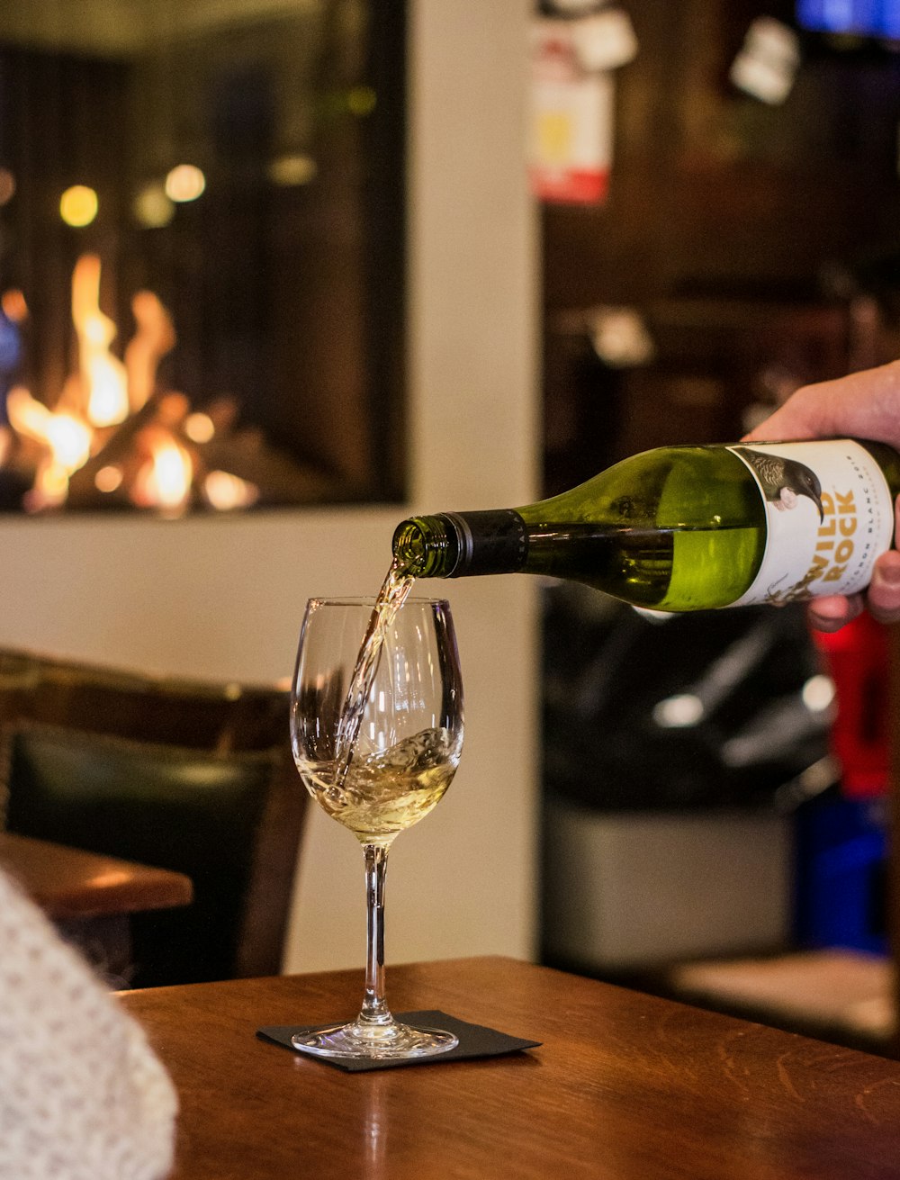 person pouring champagne on clear wine bottle