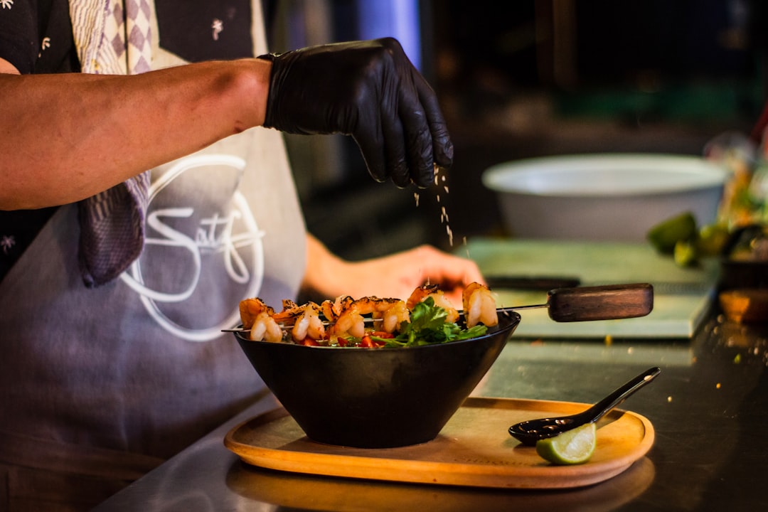 person pouring seasoning on bowl of food