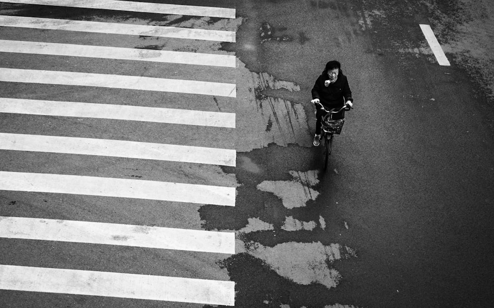 grayscale photo of woman riding bicycle near pedestrian lane