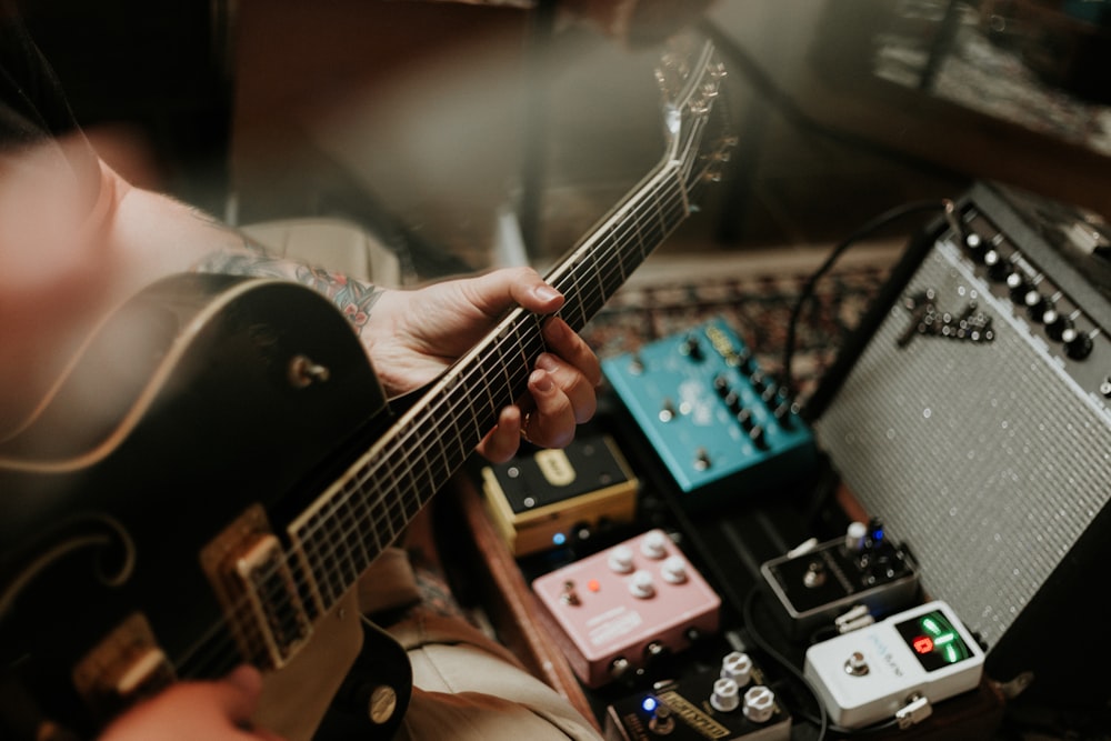 person playing guitar near guitar pedals and amplifier