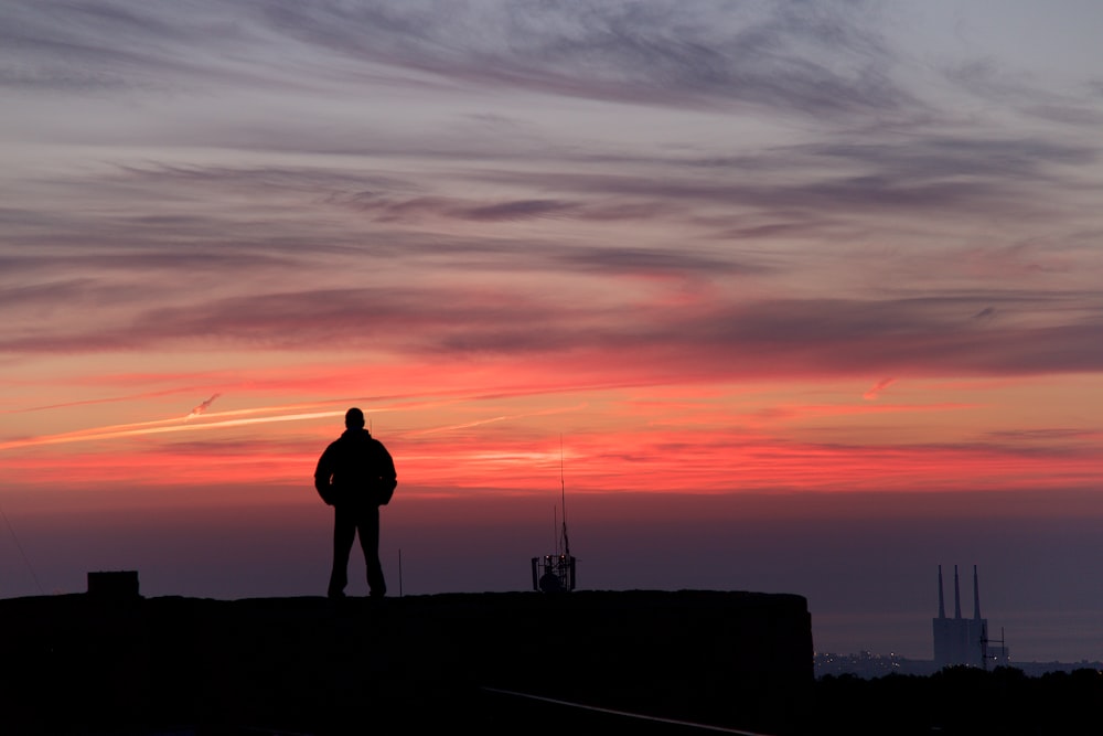 Un hombre parado en lo alto de un techo al atardecer