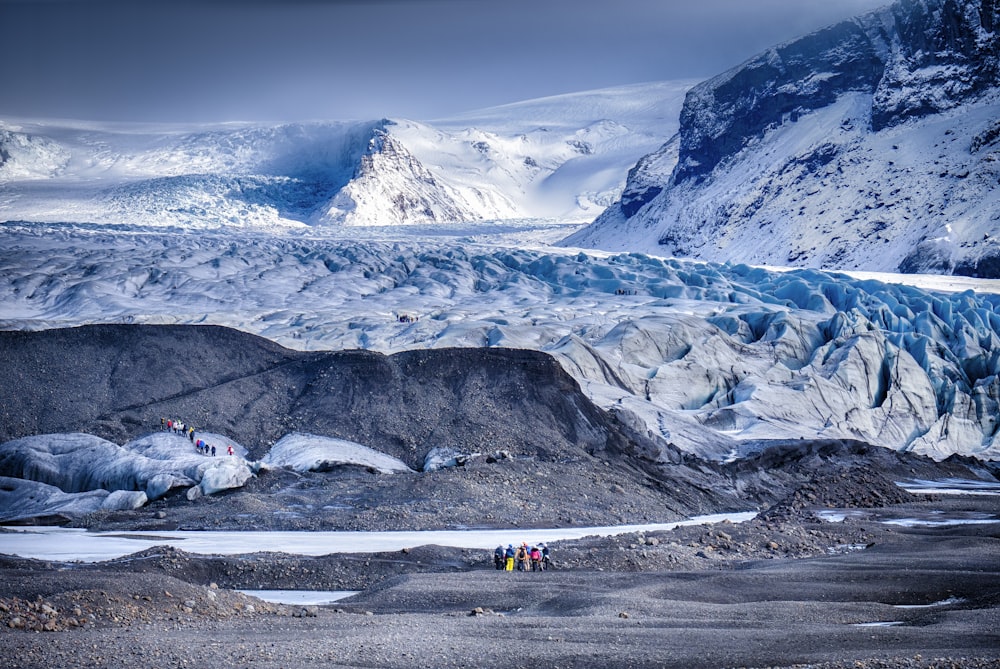 people near body of water viewing mountain covered with snow under white and blue sky