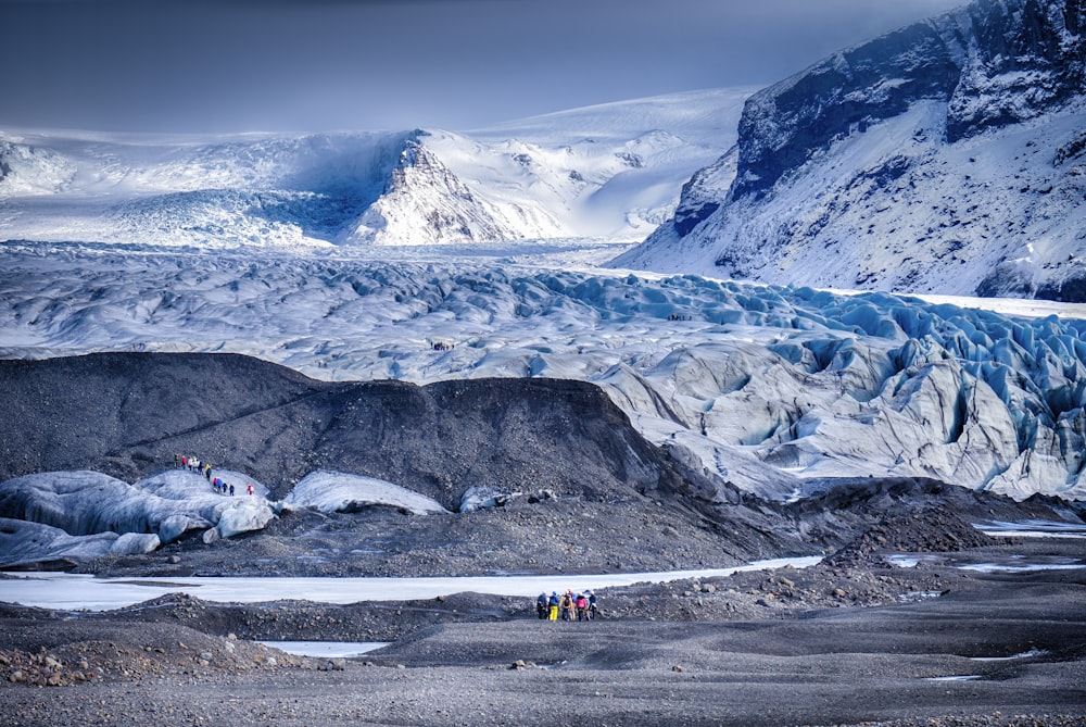 personnes près du plan d’eau vue montagne couverte de neige sous ciel blanc et bleu