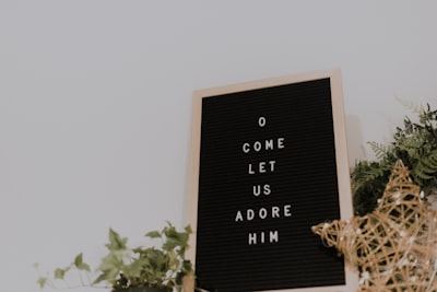 shallow focus photo of come let us adore him quote board with brown wooden frame carols google meet background