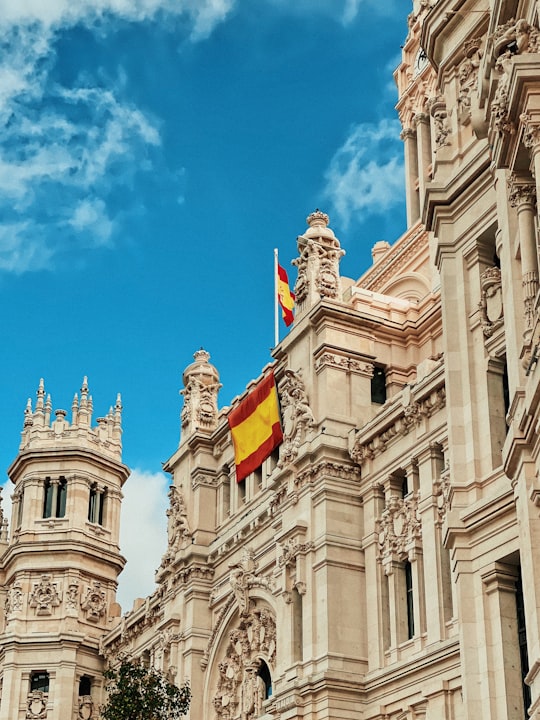 yellow and red flag hanging on white building in Fuente de Cibeles Spain