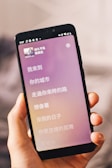 A hand is holding a smartphone displaying song lyrics in Chinese. The phone screen shows a music app with a pink and purple gradient background. The status icons like battery and WiFi are visible at the top.