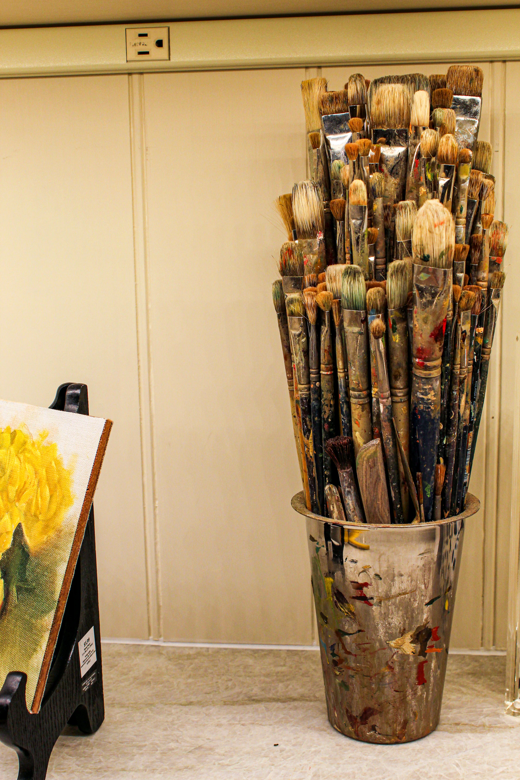 An artist’s working collection of paint-covered brushes beside a painting