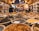 A vibrant market scene with numerous bowls filled with diverse spices and herbs, neatly arranged in rows. The market is bustling with activity, with a person blurred in the background walking past various other stalls filled with goods. Warm lighting creates an inviting and cozy atmosphere.