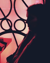 A silhouette of a person in profile against a bright geometric background composed of circular and intersecting lines. The image features stark contrasts between dark shadows and the illuminated backdrop, creating a striking visual effect.