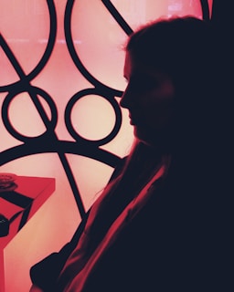 A silhouette of a person in profile against a bright geometric background composed of circular and intersecting lines. The image features stark contrasts between dark shadows and the illuminated backdrop, creating a striking visual effect.