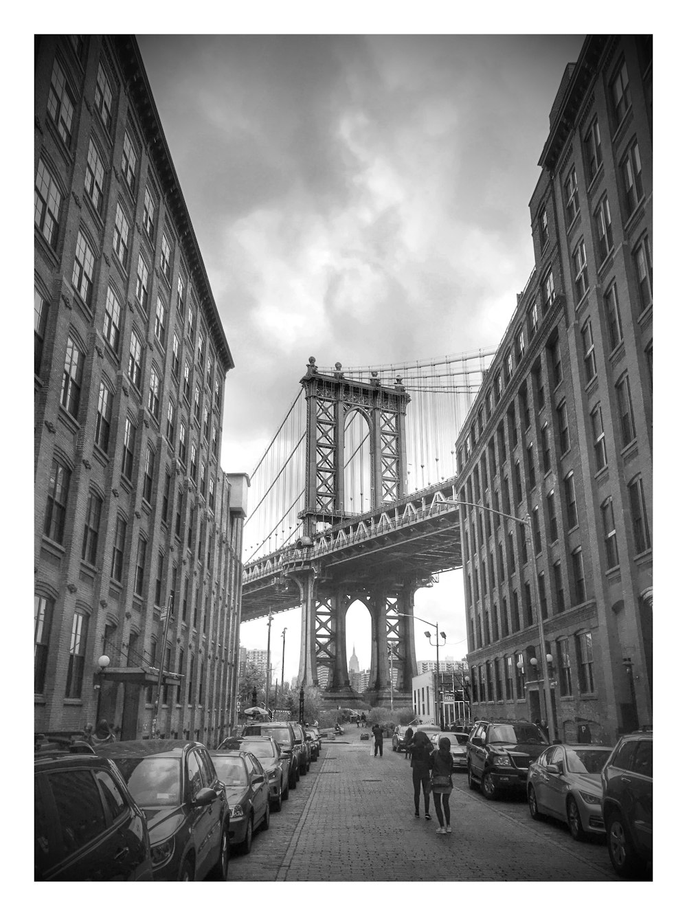 grayscale photography of people near vehicles and buildings and bridge