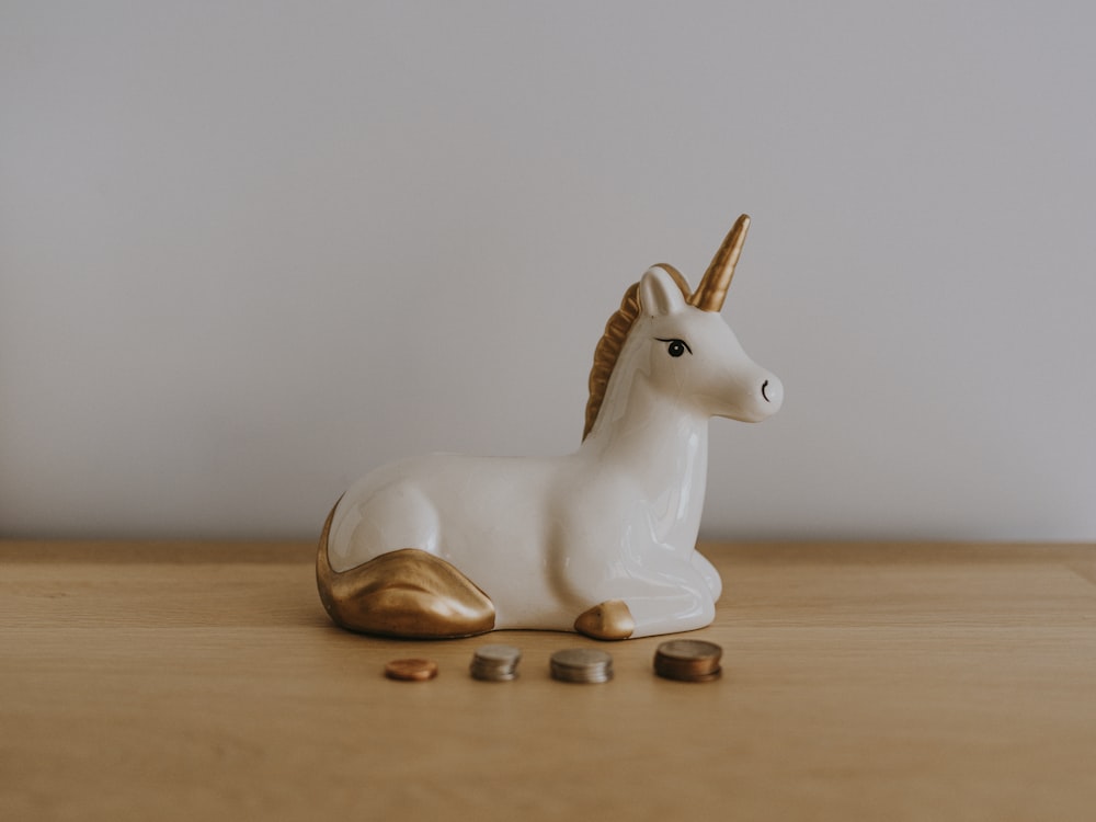 Figura de unicornio de cerámica blanca y dorada cerca de monedas