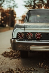 Vintage car parked on a rustic country road surrounded by autumn leaves.