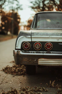 A polished vintage car parked along a country road lined with autumn leaves