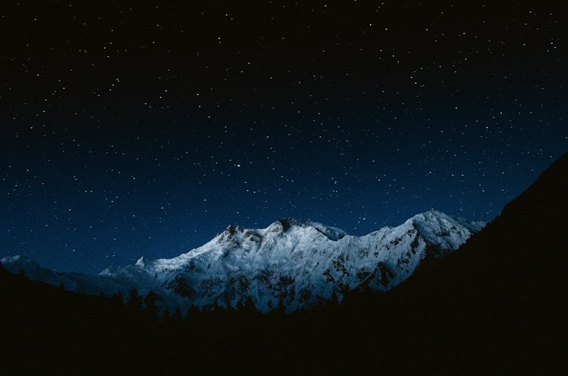 A snow-covered mountain peak under a dark night sky filled with bright stars