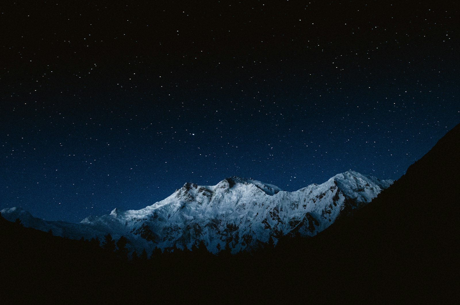 A snow-covered mountain peak under a dark night sky filled with bright stars