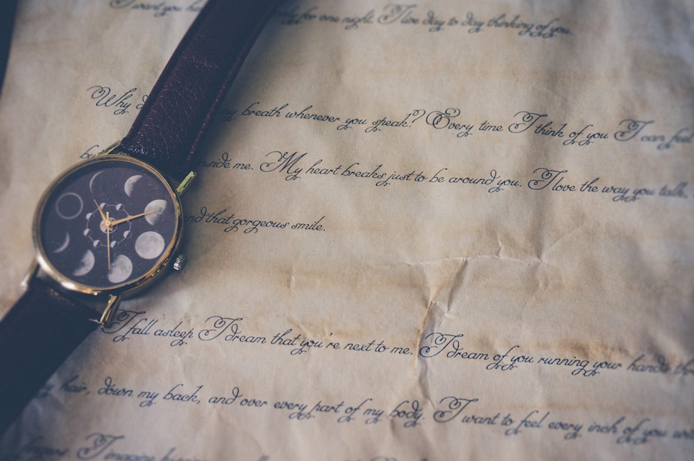 round black and gold-colored analog watch with brown leather band on printer paper