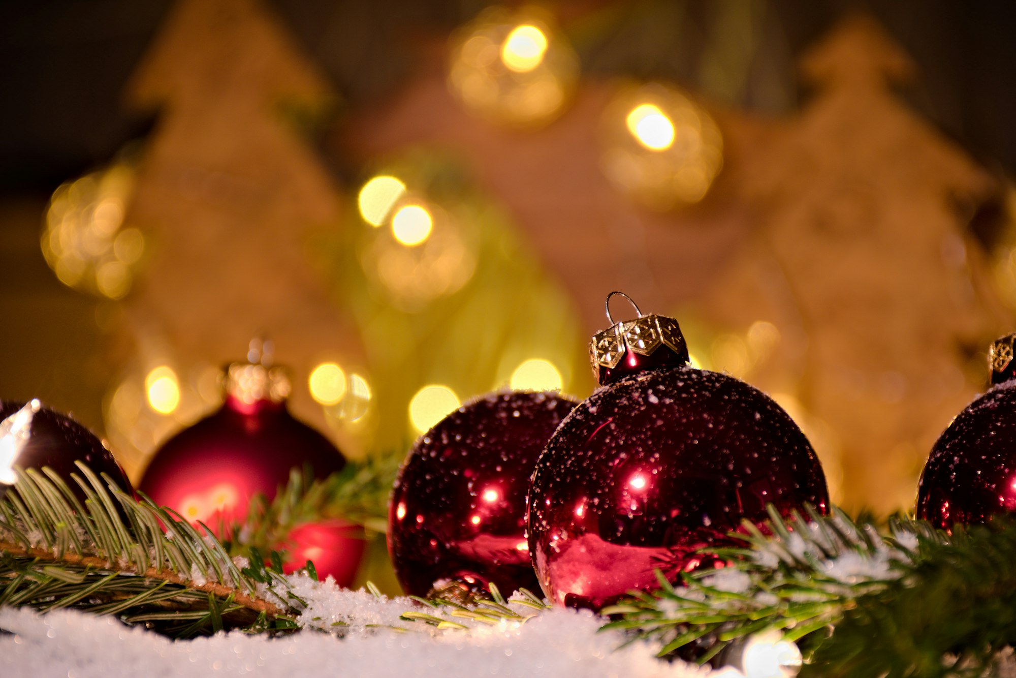 Red ornaments on snow and pine, illuminated by lights and trees.