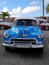 A colorful vintage car driving along a scenic Cuban coastal road with palm trees and blue skies.