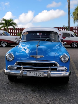 A colorful vintage car driving along a scenic Cuban coastal road with palm trees and blue skies.