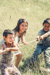 three kids pulling on a rope during daytime