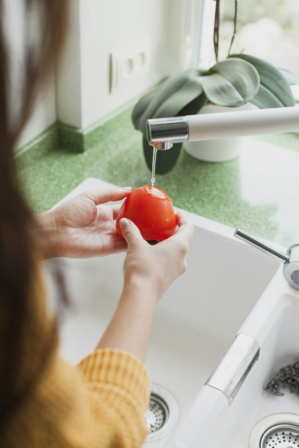 Person mit roter Tomate, die im Wasserhahn gewaschen wird