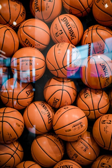A close-up of a variety of sports balls including basketballs, soccer balls, and tennis balls arranged neatly on a wooden table.
