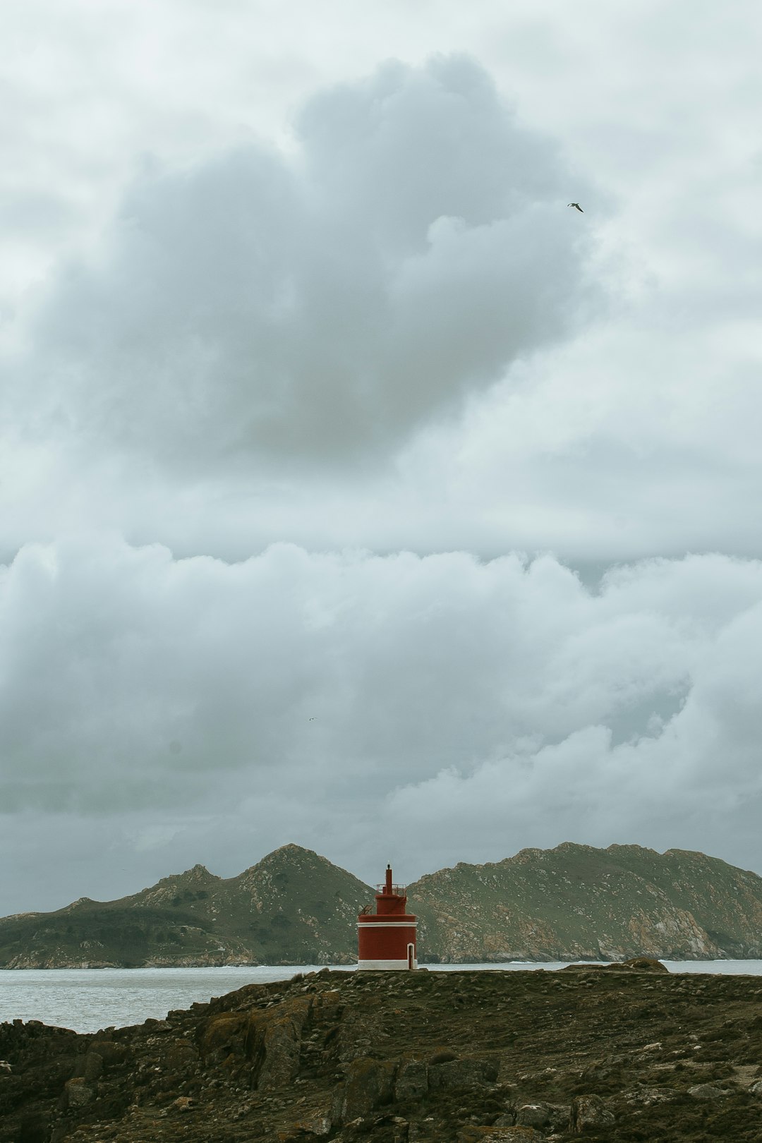 red lighthouse on cliff under cloudy sky