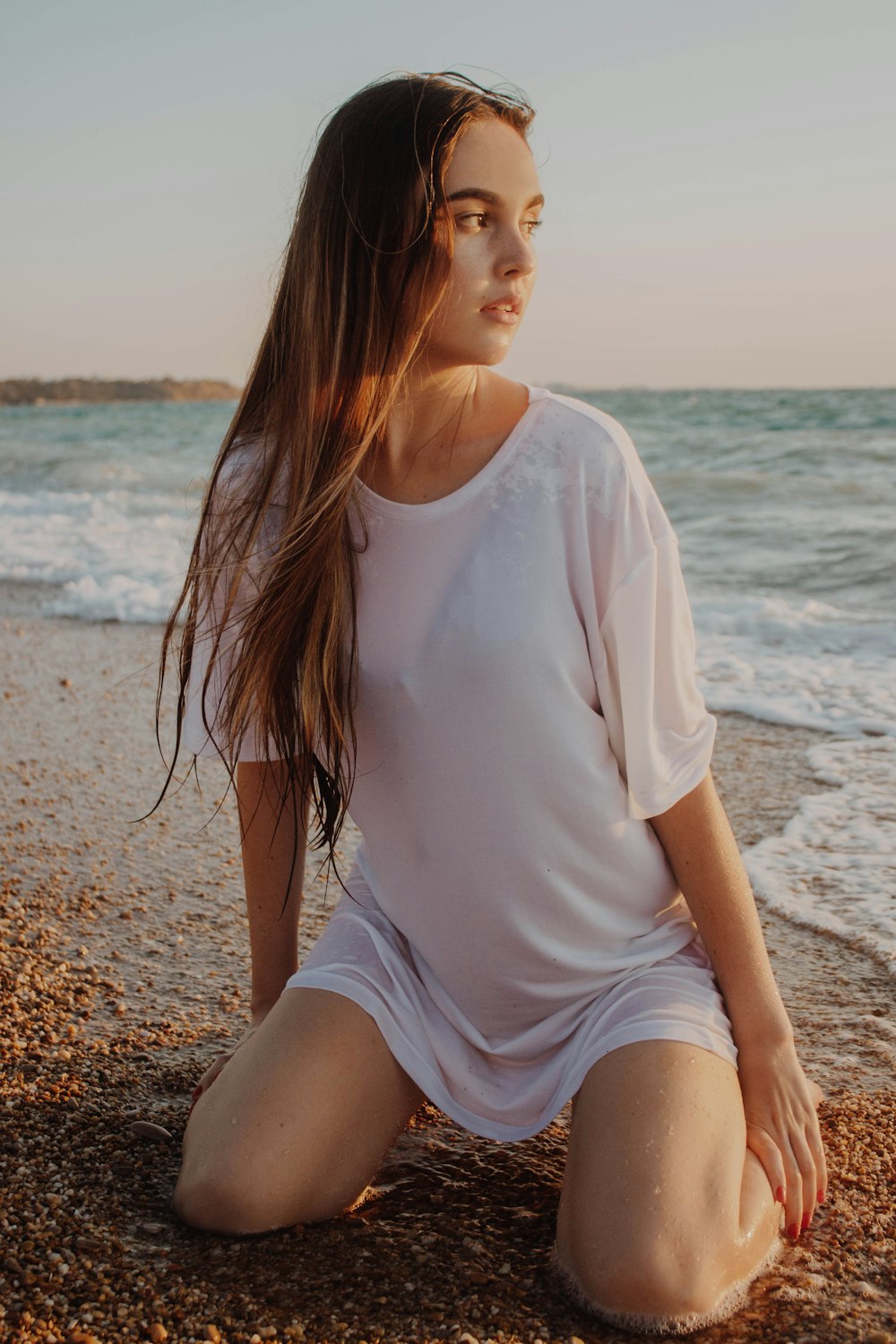 woman wearing white shirt kneeling on seashore during daytime