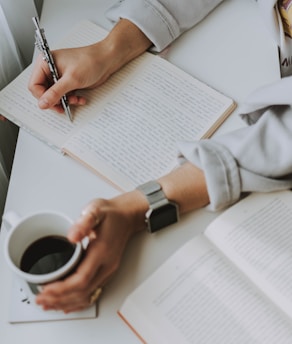 A writer at a desk typing on a laptop surrounded by notes and coffee.