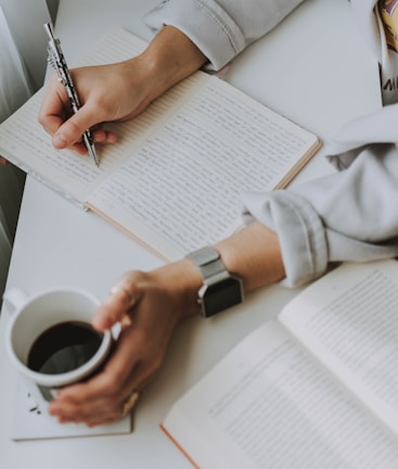 A person writing content on a notepad with a coffee cup.