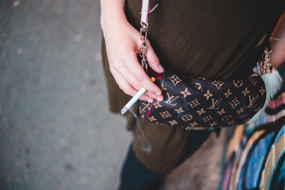 selective focus photo of person holding monogrammed Louis Vuitton crossbody bag and cigarette