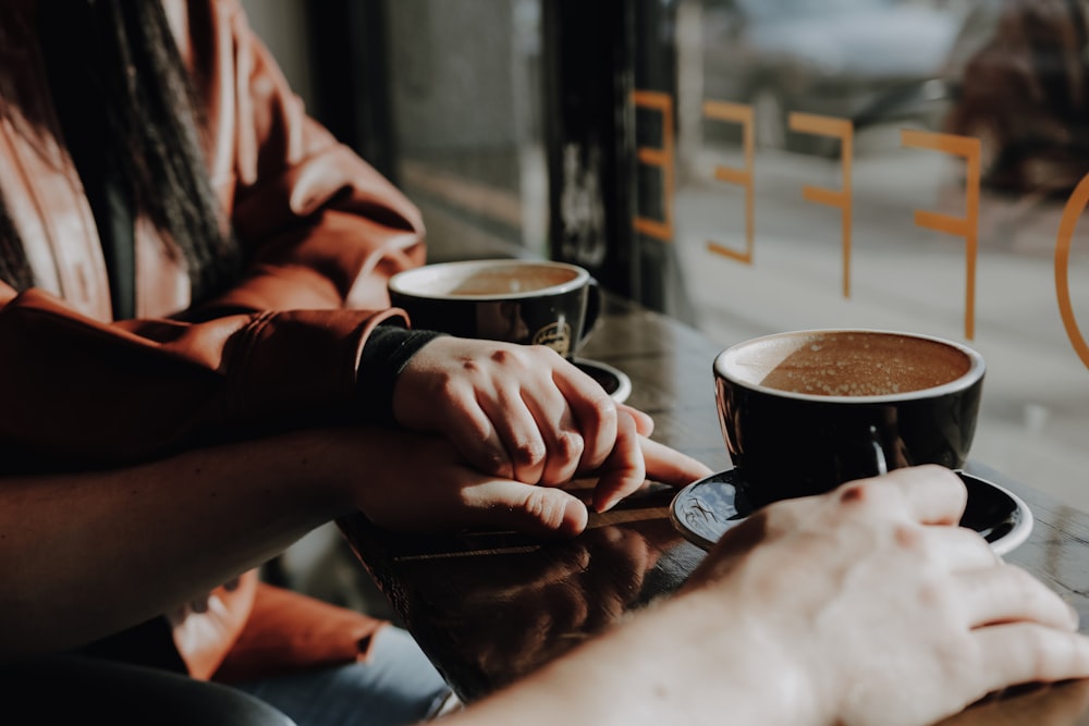 two person sitting beside window with mugs