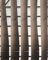 A series of vertical, parallel architectural panels or slats with a metallic finish allowing some light through, set against a grid-like backdrop.
