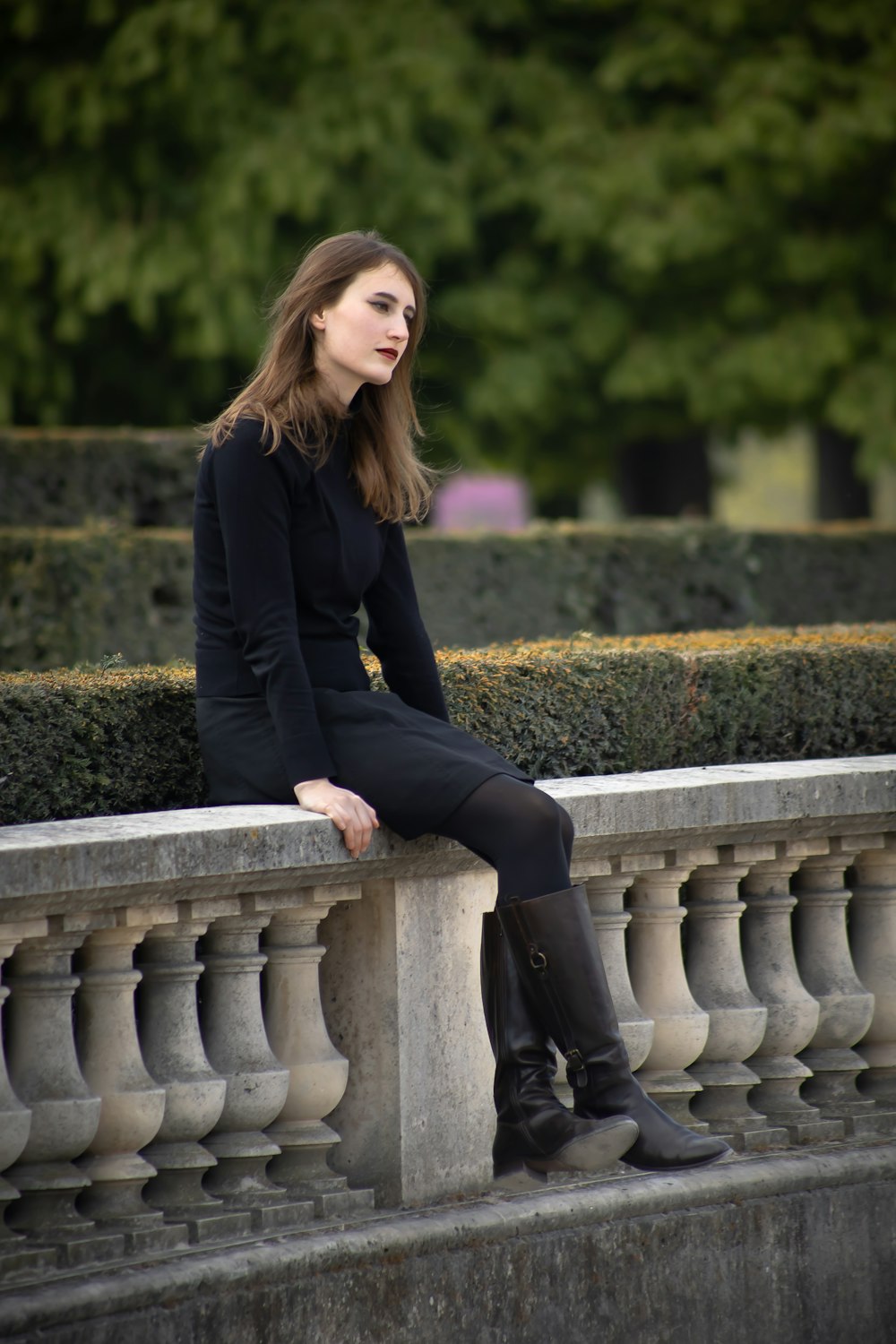 woman wearing black dress sitting on ballast fence