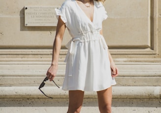 woman in white V-neck cap-sleeved mini dress standing near wall