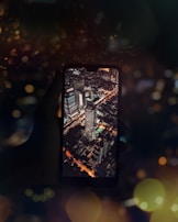A hand holding a smartphone with a glowing screen against a cityscape at night.