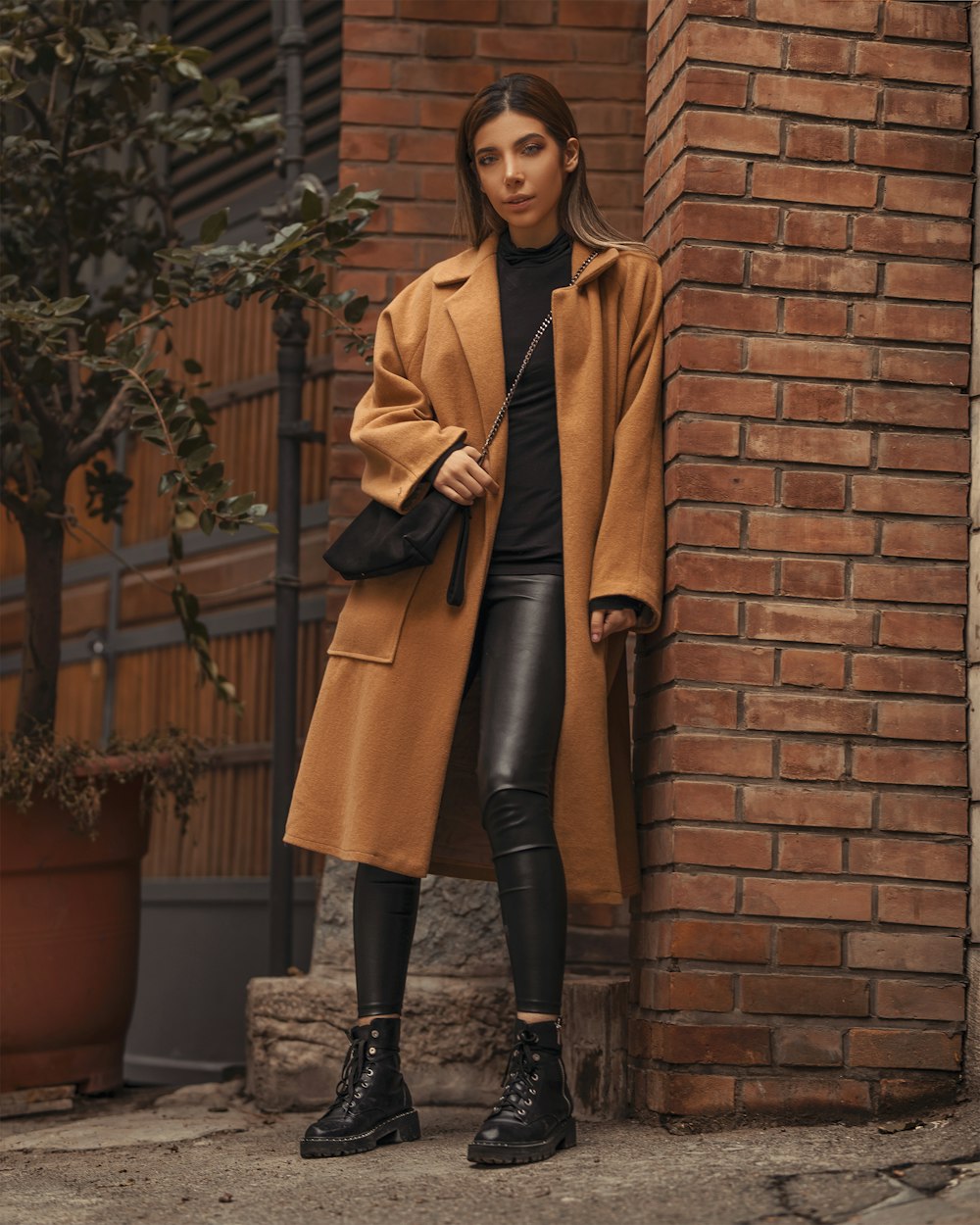 woman in brown overcoat leaning on wall
