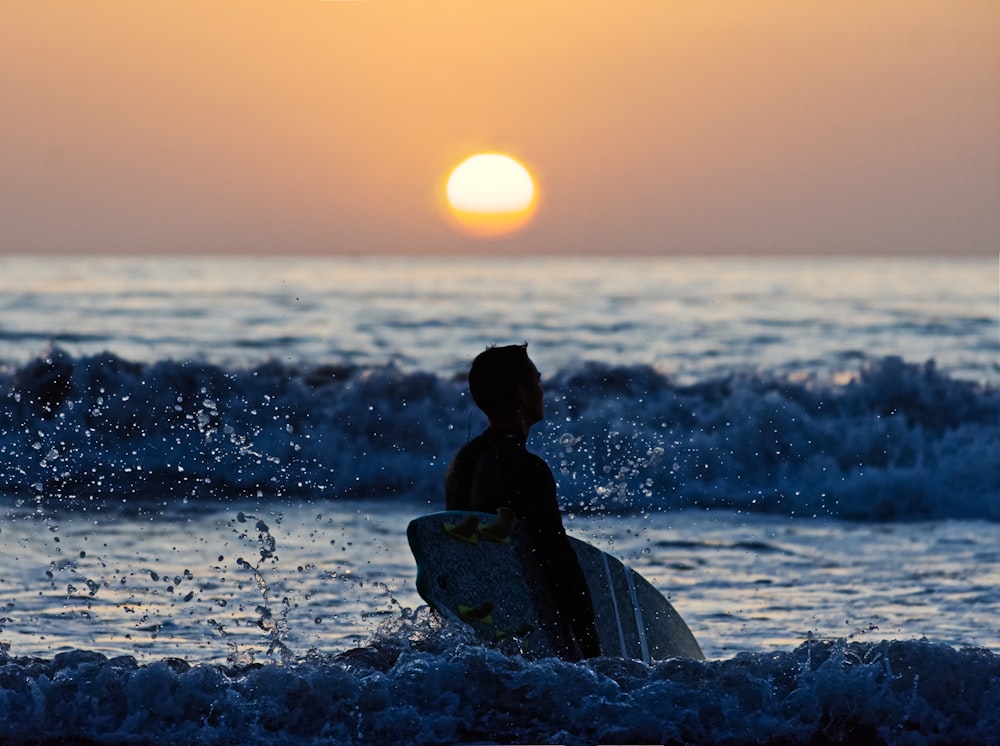 selective focus photo of man holding surfboard with sea waves about to crash on shore